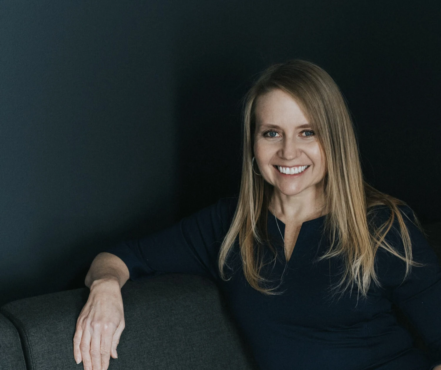 Roxie seated on a couch, smiling, in a relaxed professional portrait.